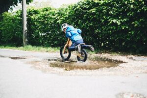 Criança passando em poça com bicicleta de equilíbrio.